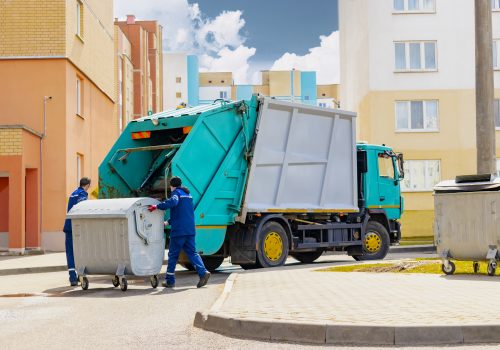 an automobile garbage truck collects garbage in residential areas of a modern city. men load a metal container with garbage into a car for collecting and transporting garbage.