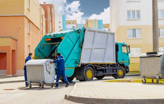 an automobile garbage truck collects garbage in residential areas of a modern city. men load a metal container with garbage into a car for collecting and transporting garbage.
